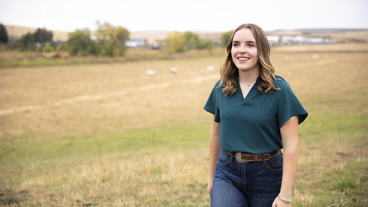 A woman walks in a pasture with cows in the background.