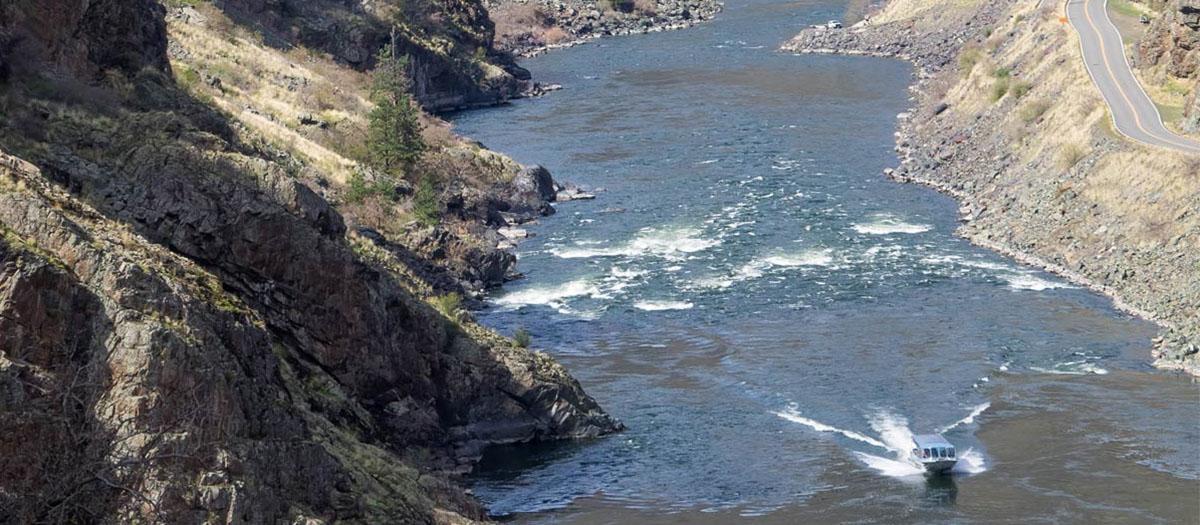 A small boat in the corner leaves a wake in the water between two steep banks.